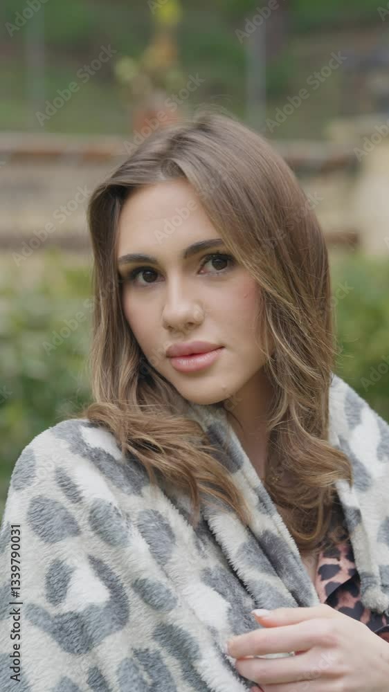 A young woman with wavy brown hair and light skin is wrapped in a soft blanket. She gazes at the camera with a calm expression. The blurred background features warm autumn tones, creating a serene A young woman with wavy brown hair and light skin is wrapped in a soft blanket. She gazes at the camera with a calm expression. The blurred background features warm autumn tones, creating a serene