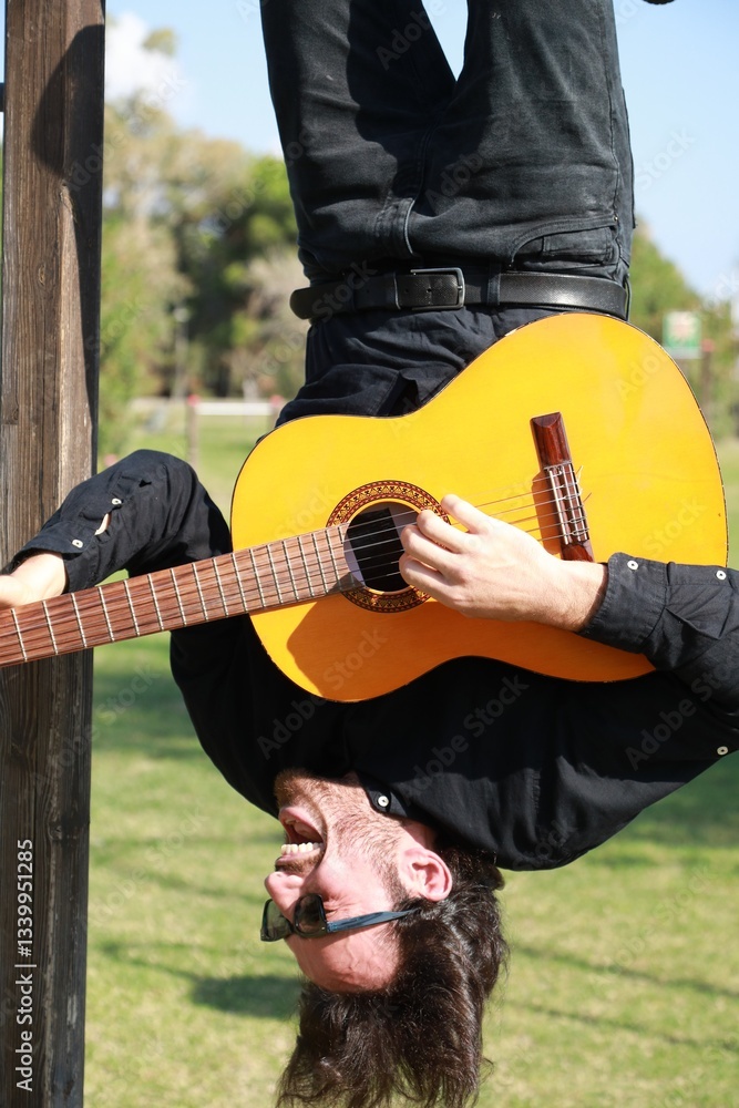Young Man Plays Guitar Music Hanging Upside Down In An Outdoor Park Young Man Plays Guitar Music Hanging Upside Down In An Outdoor Park