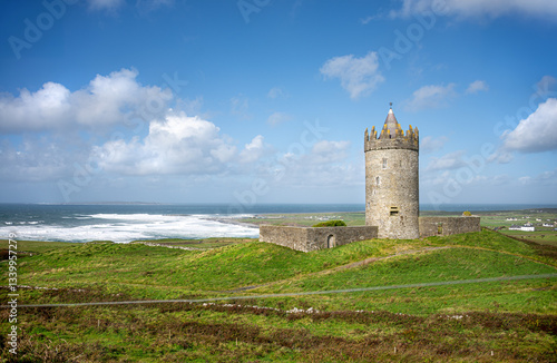 Doonagore Castle, the 16th-century cylindrical tower house near Doolin Point, looks out over the wind-blown waves of the Atlantic Ocean toward Inisheer Island on a summer day in County Clare, Ireland.