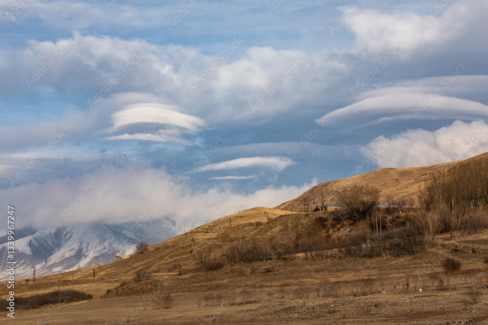 Lenticular clouds weather phenomenon over the landscapes of Syunik (Zangezur), Armenia. These unique cloud formations create a dramatic and atmospheric scene over rolling hills and open skies. Lenticular clouds weather phenomenon over the landscapes of Syunik (Zangezur), Armenia. These unique cloud formations create a dramatic and atmospheric scene over rolling hills and open skies.