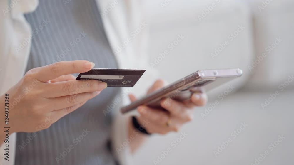 A woman is using her phone to pay for something with a credit card. She is holding the credit card in one hand and the phone in the other A woman is using her phone to pay for something with a credit card. She is holding the credit card in one hand and the phone in the other