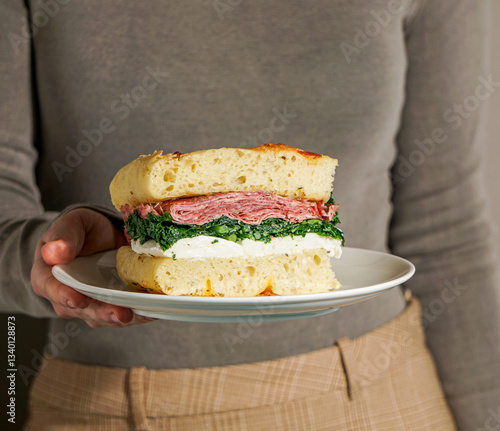 woman hand holding a focaccia bread italian sandwich, Porchetta meat, kale, mozzarella, pesto, sun light modern, neutral background
