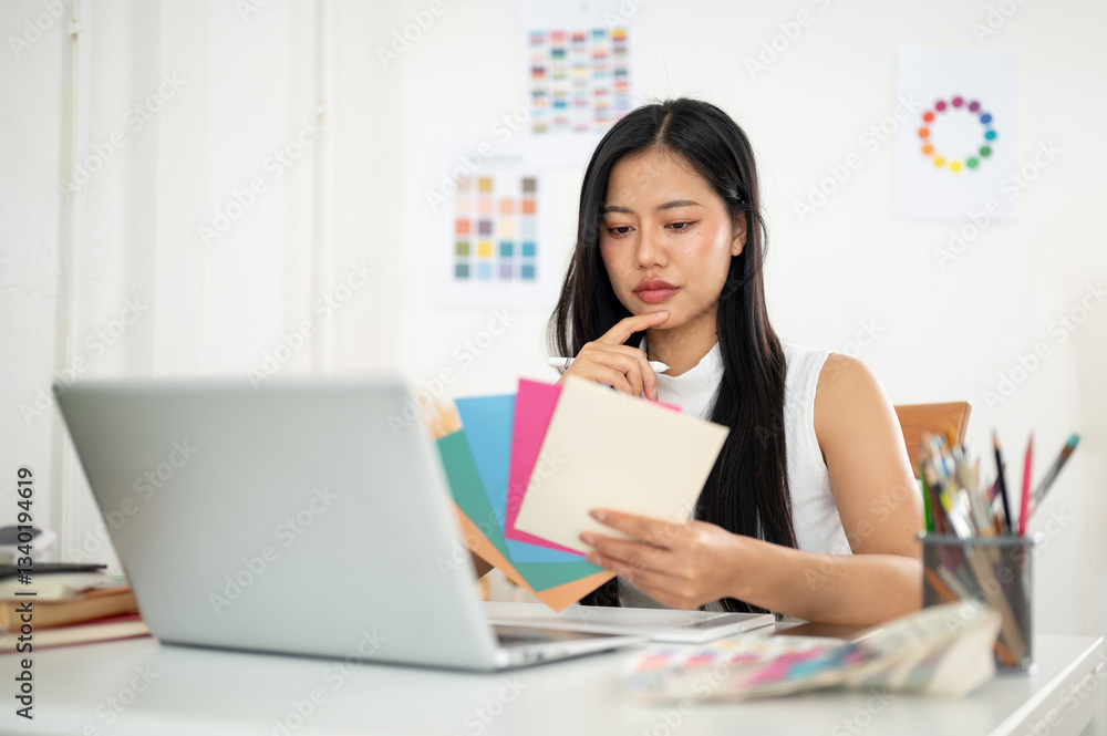 Asian woman is thinking deeply while choosing the color from color charts. Designer at work. Asian woman is thinking deeply while choosing the color from color charts. Designer at work.