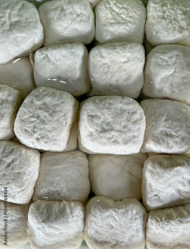 Square tofu pieces soaking in water sale on traditional market. That tofu showing their soft, textured surfaces and uniform arrangement. Square tofu pieces soaking in water sale on traditional market. That tofu showing their soft, textured surfaces and uniform arrangement.