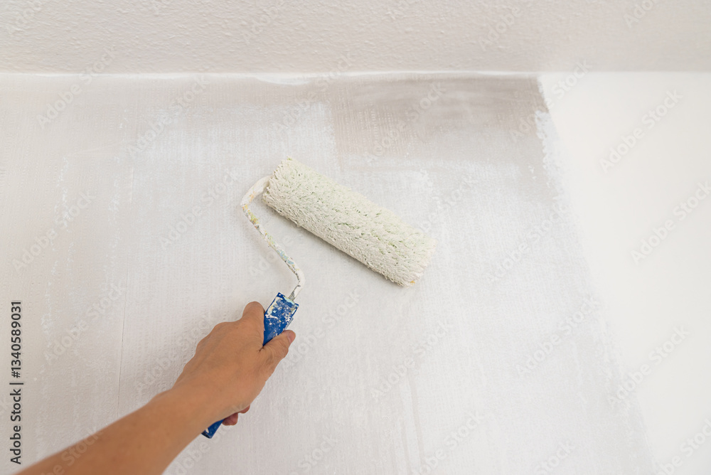 womans hand with paint roller, saturated with white dispersion paint. renovating the wall from smoke.