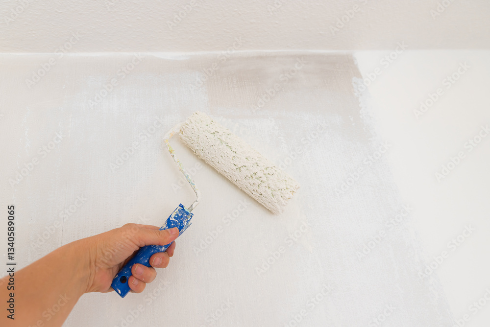 womans hand with paint roller, saturated with white dispersion paint. renovating the wall from smoke