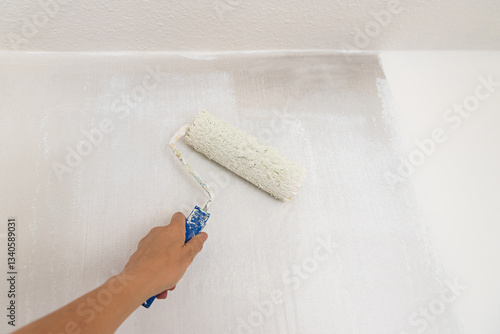 womans hand with paint roller, saturated with white dispersion paint. renovating the wall from smoke.
