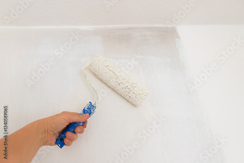 womans hand with paint roller, saturated with white dispersion paint. renovating the wall from smoke