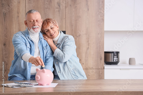 Mature couple putting coin into piggy bank in kitchen