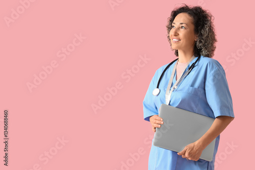 Mature female doctor with laptop on pink background