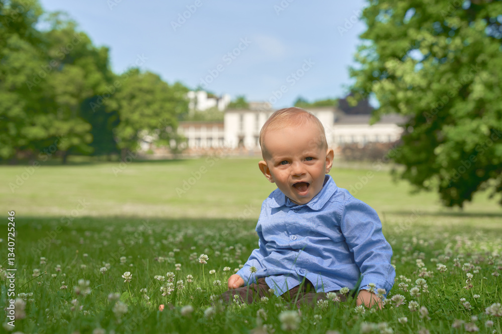 boy up to one year old European appearance blue eyes sits in the summer on a green meadow with small white flowers and wearing a blue shirt boy up to one year old European appearance blue eyes sits in the summer on a green meadow with small white flowers and wearing a blue shirt