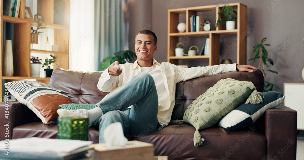Fototapeta premium Man, watching tv and happy on sofa, remote or choice for show, film or sports in living room at apartment. Person, smile and streaming subscription with movies, relax and laughing on couch in home