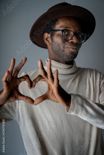 Obraz na płótnie Smiling Black man with glasses and hat making heart shape with hands
