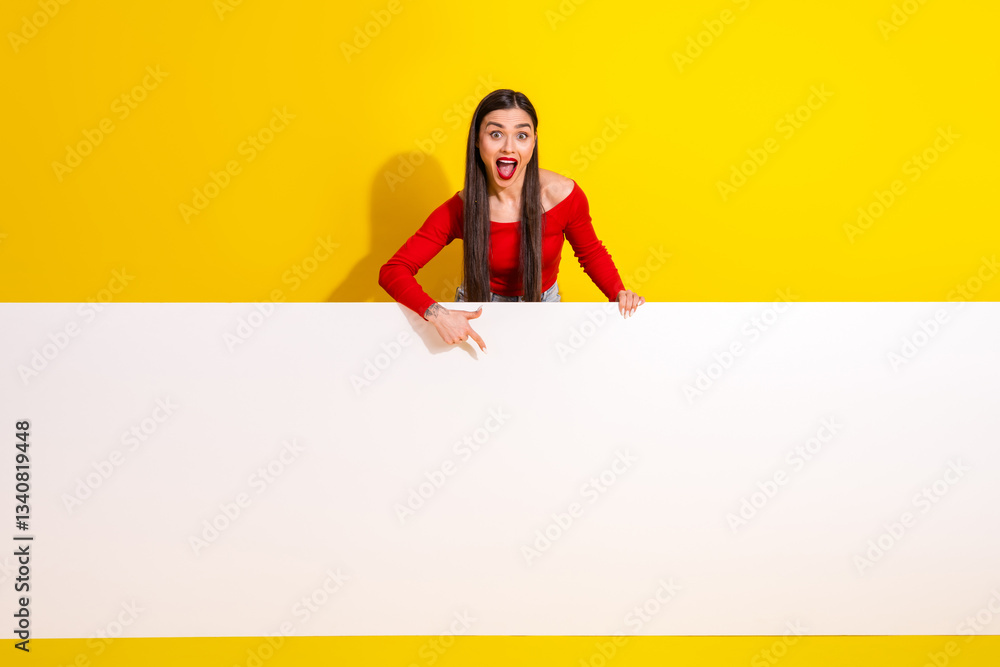 Cheerful young woman in trendy red outfit pointing and expressing surprise against a vibrant yellow background with a blank white banner Cheerful young woman in trendy red outfit pointing and expressing surprise against a vibrant yellow background with a blank white banner