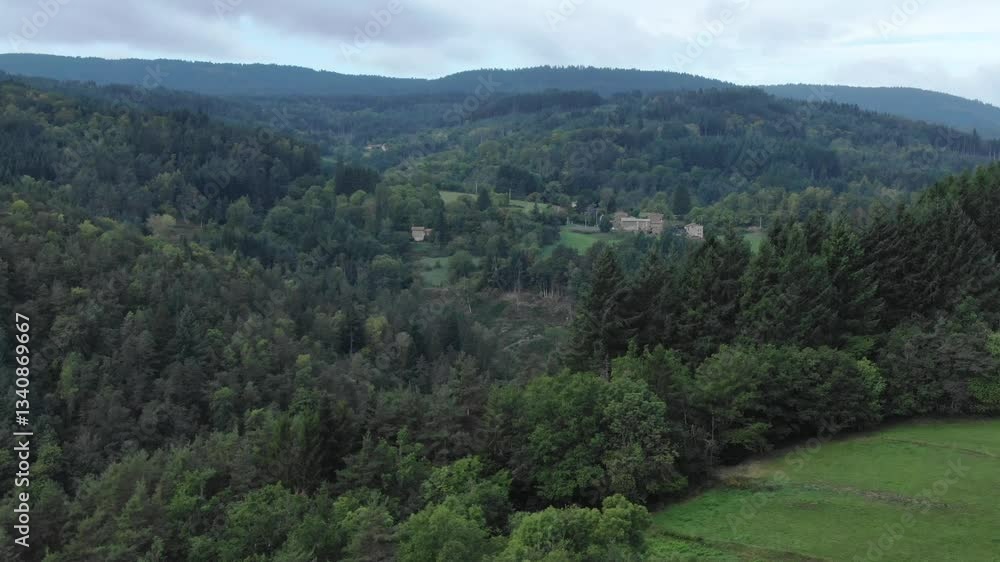 Aerial view of green valley with lush hills and distant village, Ambert, France. Aerial forward Aerial view of green valley with lush hills and distant village, Ambert, France. Aerial forward