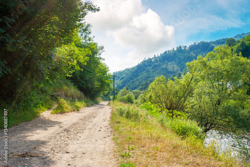 Obraz na płótnie rural landscape with road in summer. countryside nature with mountain in background. rustic scenery with green grass on hill and blue sky. scenic view of gravel ground street in valley w salonie
