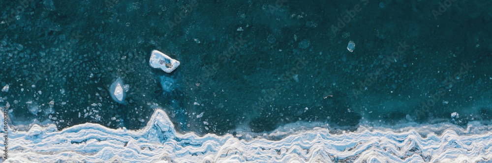 Top view of the freezing sea. Winter aerial photograph of the icy coast and ice floes in sea water. Northern nature. Cold frosty winter weather. Arctic climate. Beautiful wide panoramic background.