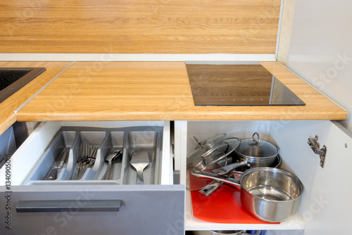 Obraz na płótnie An open kitchen cabinet. The drawer for cutlery contains forks and spoons. There are pots on the shelves. An electric kitchen stove (cooking hob) built into the countertop. Kitchen furniture. w salonie