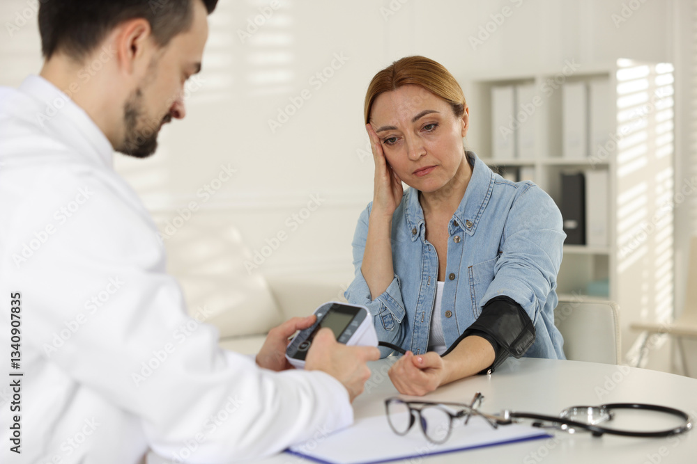 Cardiologist measuring patient's blood pressure at table in hospital Cardiologist measuring patient's blood pressure at table in hospital