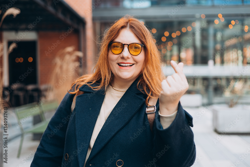 Female hand showing finger heart or mini heart gesture with the index finger and thumb come together like a snap outdoors. 30s Woman in sunglasses on urban background. High quality photo.