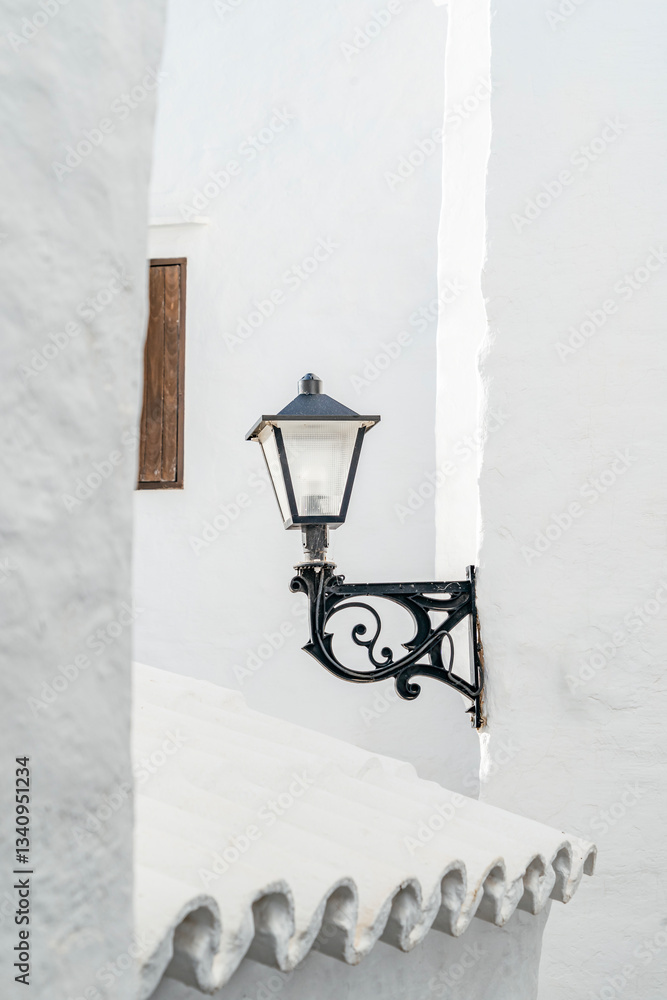 Capture the essence of Menorca with this image of a vintage lantern on a white wall, showcasing architectural detail and rustic charm. Architectural, travel, decorative themes. Binibeca Vell