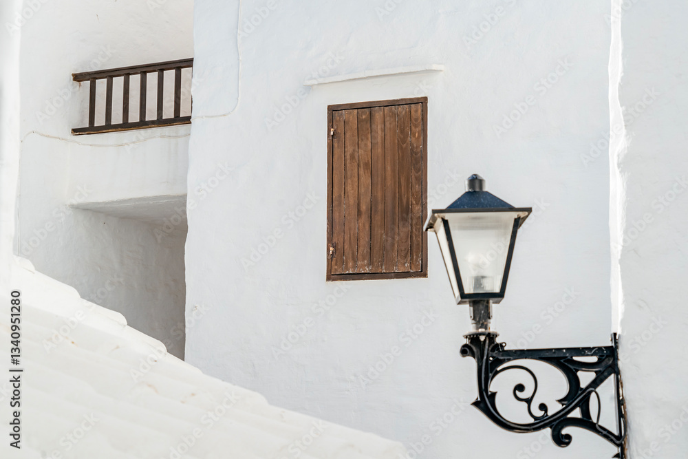 Capture the essence of Menorca with this image of a vintage lantern on a white wall, showcasing architectural detail and rustic charm. Architectural, travel, decorative themes. Binibeca Vell