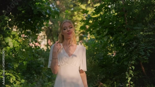 Graceful beautiful blond woman walking among lush green foliage in a soft, light dress. sunlight, serene garden, greenery softly blurred in the background. romantic and dreamy ambiance, intimate mood