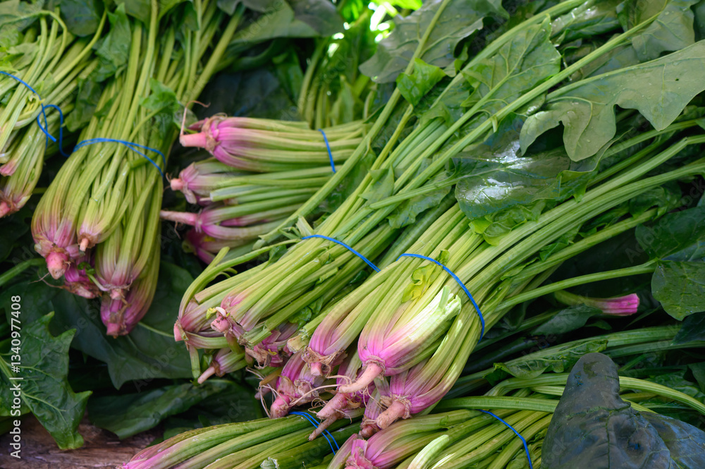 Fototapeta premium Bunches of fresh green vegetables with a hint of pink at a bustling farmers market in the early morning