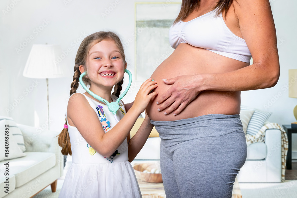 A happy girl listening with a stethoscope her mothers pregnant belly in anticipation of her baby brother or sister