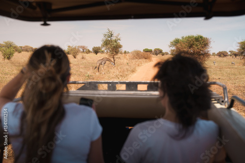 Tourists watching giraffe grazing in tarangire national park, tanzania