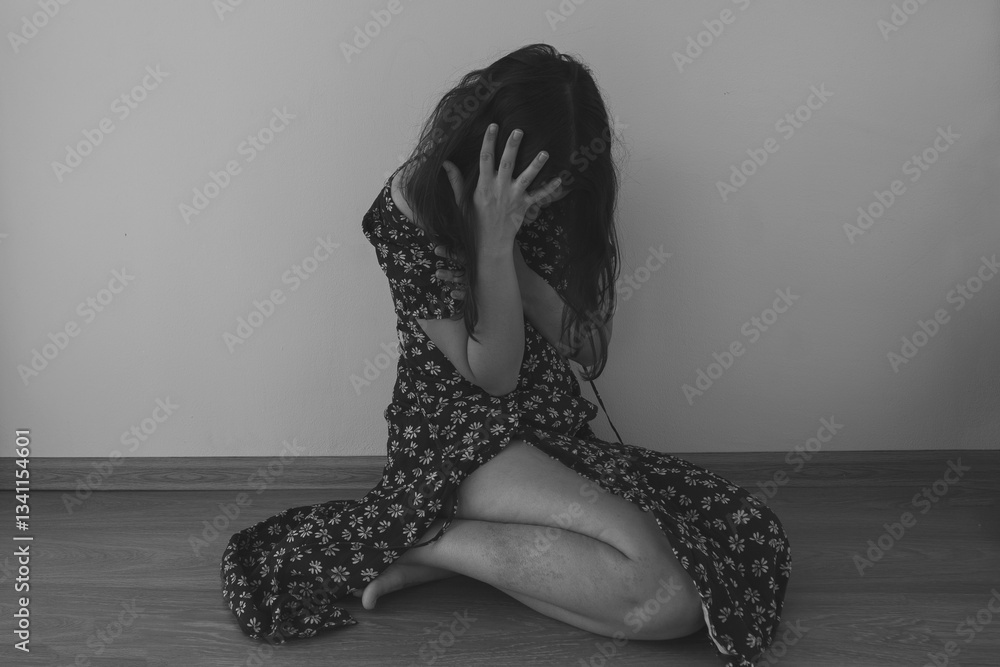 Naklejka premium black-white photo young woman in floral torn dress sitting on floor covering head and face with hands, victim of domestic violence.