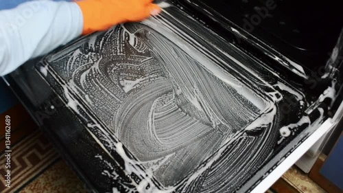 Person is cleaning a dirty oven with a brush and a sponge. The oven is covered in grease and grime, and the person is scrubbing it vigorously to remove the dirt. Concept of hard work