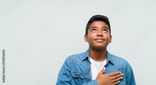 Hispanic teen male pledging allegiance with hand on heart, looking upwards