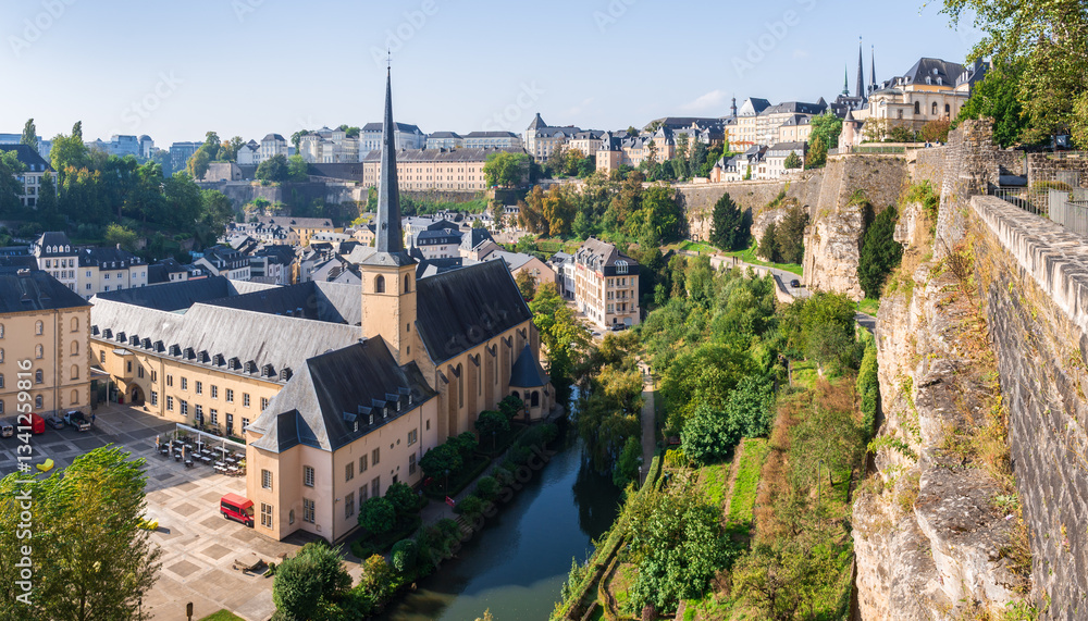 Fototapeta premium Panoramic view of the Alzette valley in Luxembourg City, Luxembourg, with the Neimënster Abbey and Grund district on the left overlooked by the Ville-Haute district, the old town, on a sunny day.
