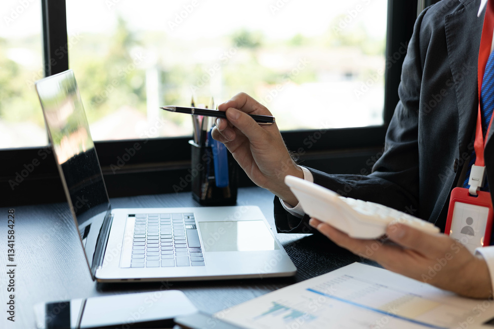 Naklejka premium A man in a suit is working on documents in an office. He holds a pen and is analyzing data. This scene conveys a professional working atmosphere. 