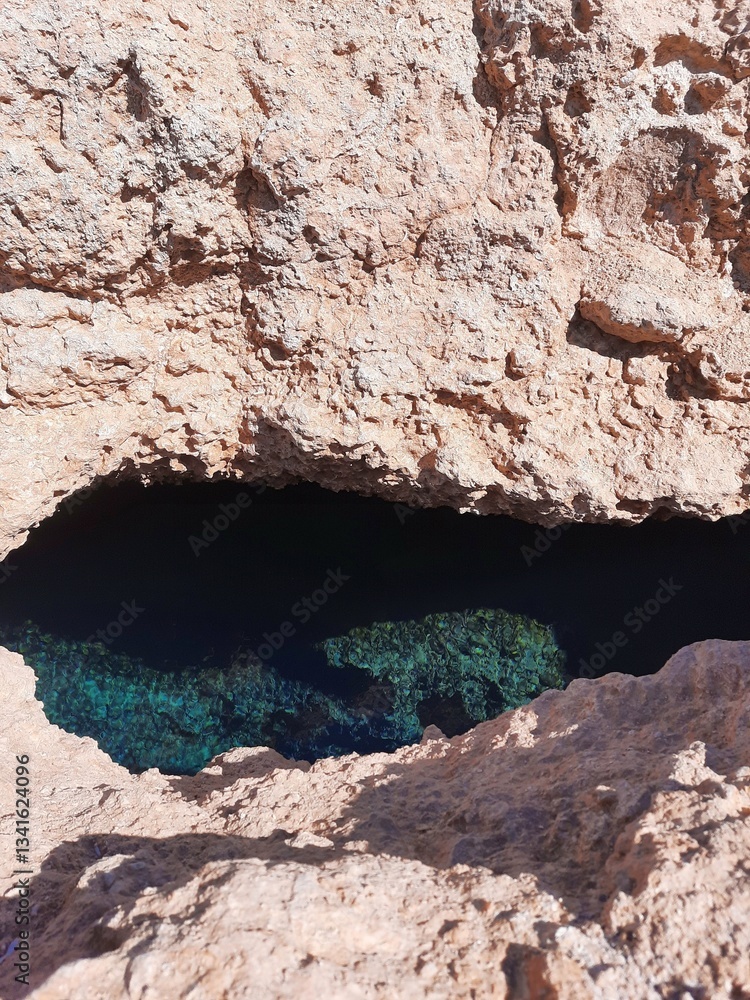 Fototapeta premium Mysterious Cave Opening with Deep Blue Water Surrounded by Rocky Cliffs