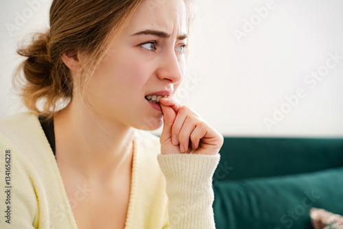 Photography Closeup of a nervous, worried young white woman biting her fingers or nails sitting on a sofa indoors