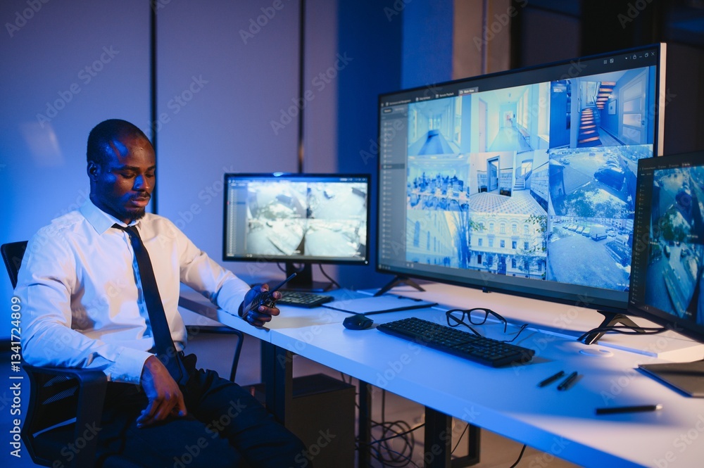 Fototapeta premium African American security guard looking at desktop computer screen while speaking on walkie talkie