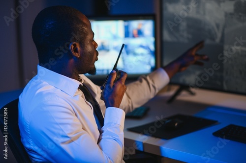 Φωτογραφία African-American security officer watching the screens talking on radio in contr