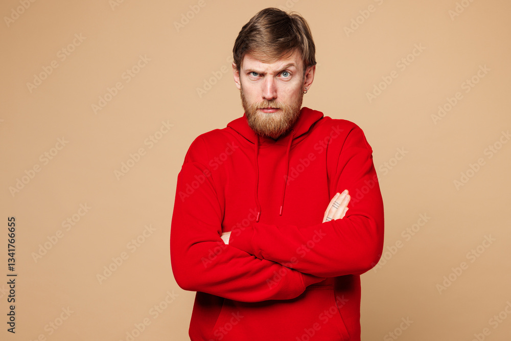 Fototapeta premium Young frowning mad sad Caucasian man he wearing red hoodie casual clothes hold hands crossed folded looking camera isolated on pastel plain light beige background studio portrait. Lifestyle concept.