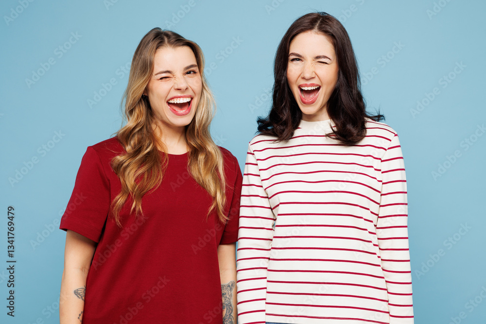 Obraz premium Young cheerful fun cool couple two friends women wearing red casual clothes look camera wink blink eye together isolated on pastel plain light blue cyan background studio portrait. Lifestyle concept.
