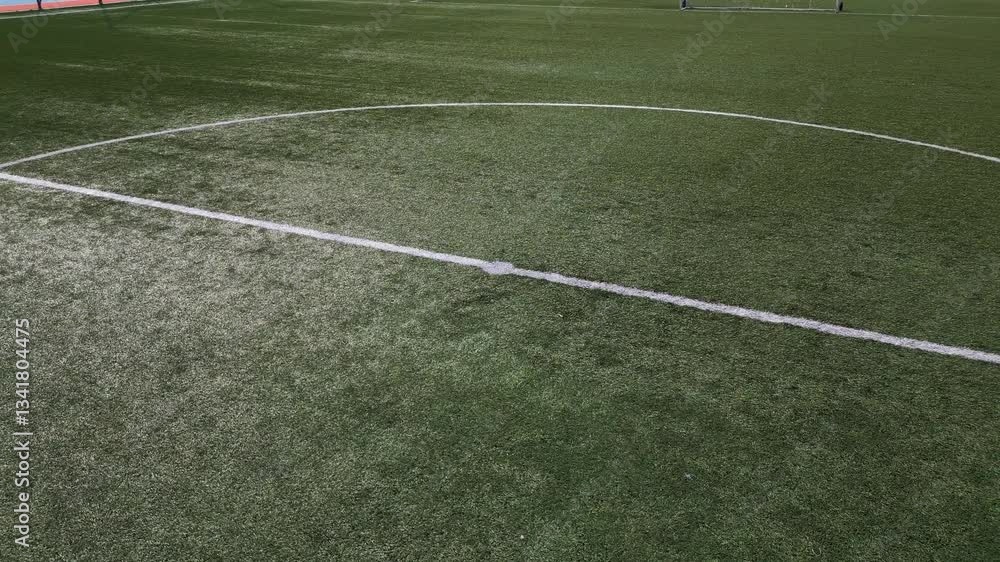 Low-altitude drone shot of an empty soccer field with artificial green grass, white boundary lines, and a goal net. The sports ground is well-maintained, creating a clean and structured composition Low-altitude drone shot of an empty soccer field with artificial green grass, white boundary lines, and a goal net. The sports ground is well-maintained, creating a clean and structured composition