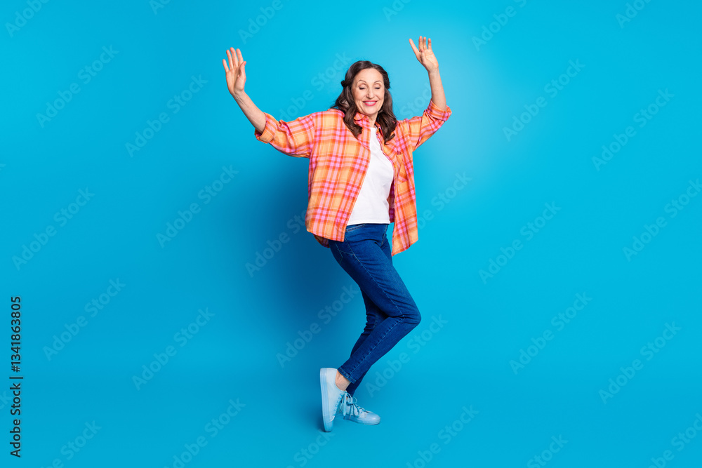 Obraz premium Joyful mature woman dancing on blue background wearing casual vibrant outfit, expressing happiness and energy