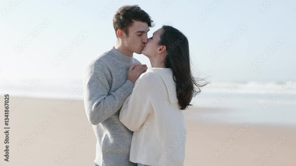 A young man and woman face each other, breathing warm air on their hands to combat the cold, sharing an intimate moment on a breezy beach day. A young man and woman face each other, breathing warm air on their hands to combat the cold, sharing an intimate moment on a breezy beach day.