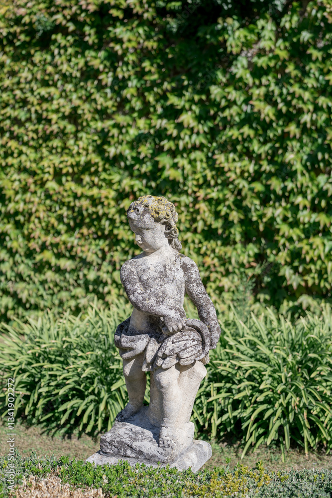 Italy, Florence - August 02, 2024: Antique sculpture of a little boy in a green garden Italy, Florence - August 02, 2024: Antique sculpture of a little boy in a green garden