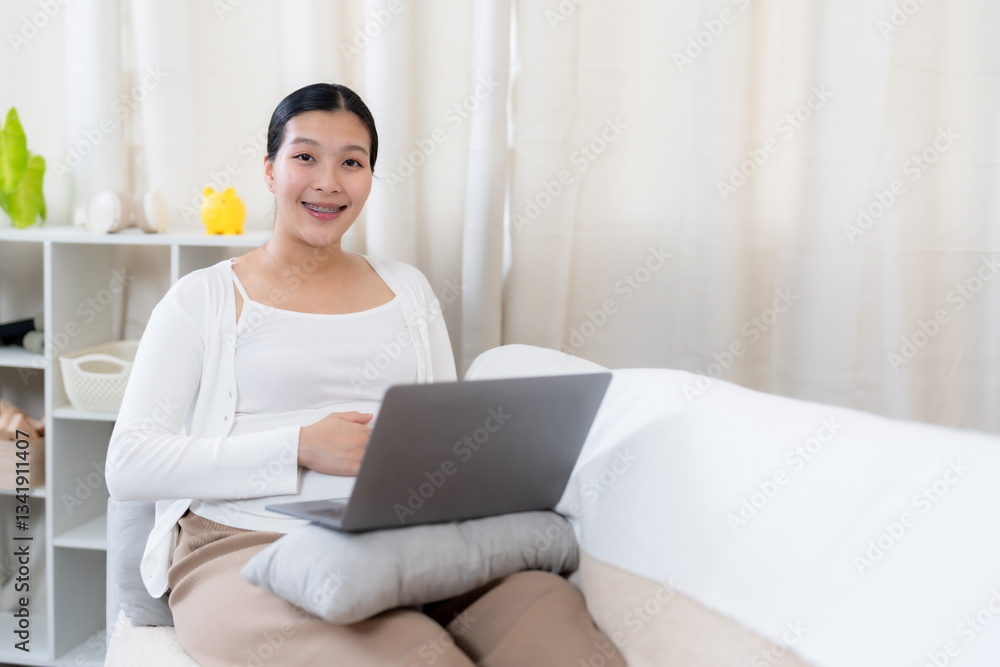 Asian pregnant woman sitting on a sofa using a laptop with a relaxed smile, enjoying a moment of productivity. Wearing a white cardigan and comfortable attire in a warm and cozy home environment. Asian pregnant woman sitting on a sofa using a laptop with a relaxed smile, enjoying a moment of productivity. Wearing a white cardigan and comfortable attire in a warm and cozy home environment.