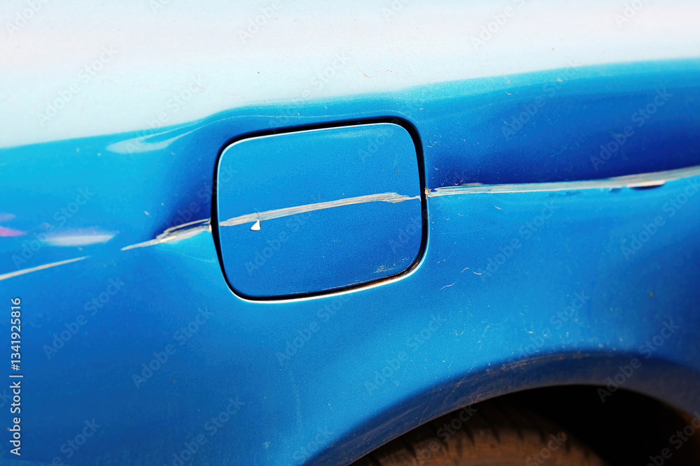Scratched fuel door on rear side of car, paint damage and surface imperfections on vehicle's body, collision aftermath, wear and tear. Visible scratches, paint damage on car fuel door. Selective focus
