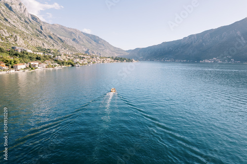 Motor yacht sails along the sea along the mountain coast. Back view