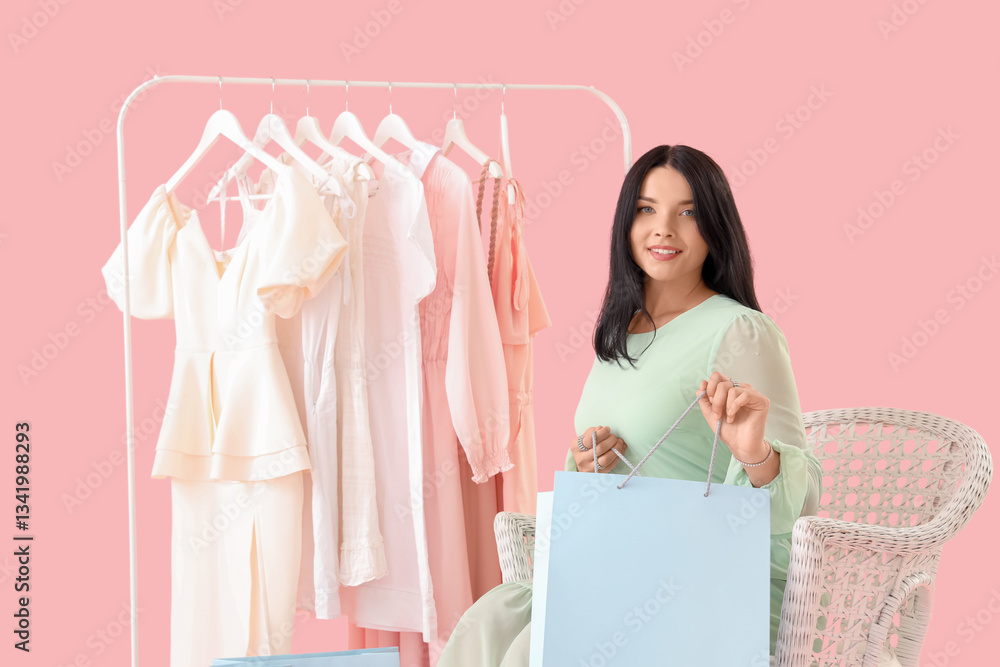 Beautiful young woman with shopping bag sitting on armchair against pink background