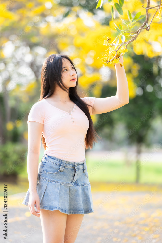 Portrait cute smiles Asian of attractive young teenage girl in Beautiful blooming Yellow Golden Tabebuia Chrysotricha flowers with the park in spring day at Evening background in Thailand.